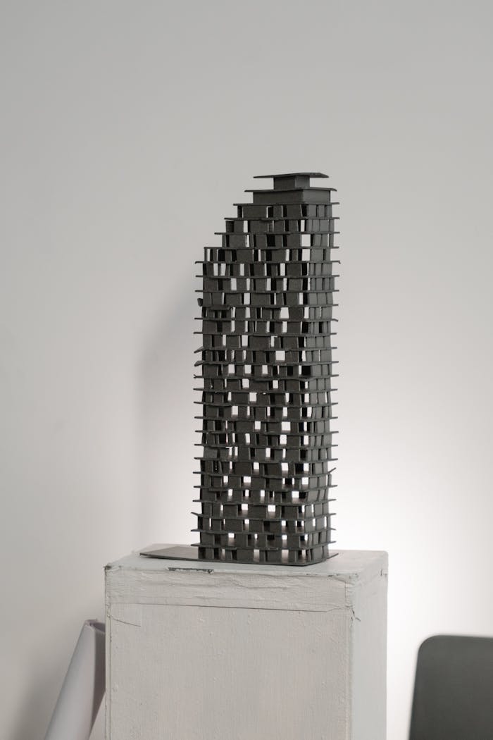 client-stories-img Abstract architectural model in gray silhouette on a white pedestal, studio background.